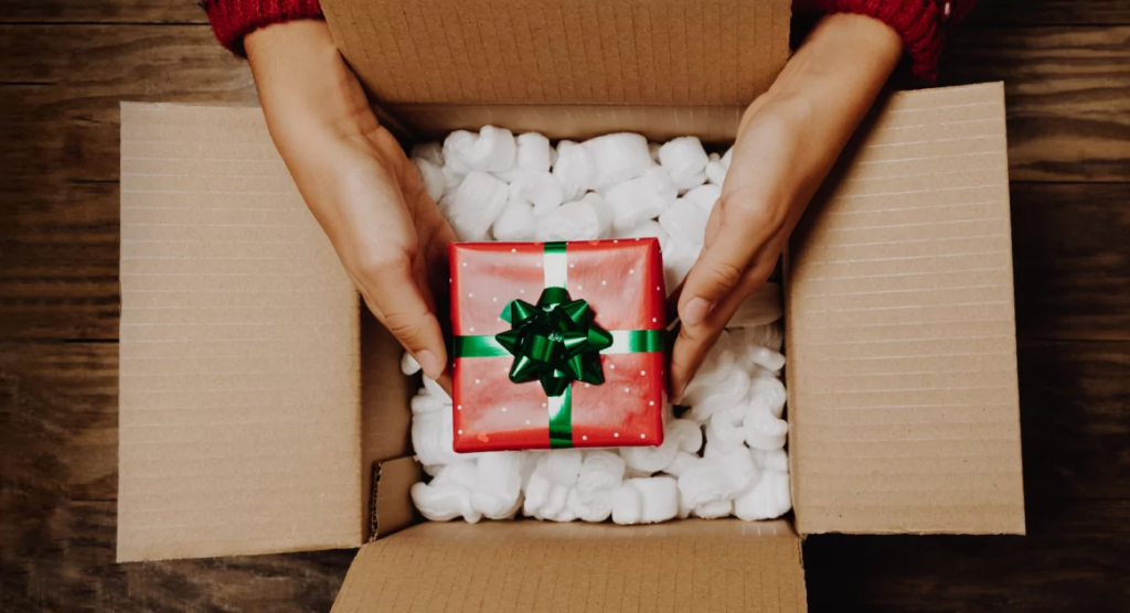 A person pulls a red and green wrapped present out of a shipping box.